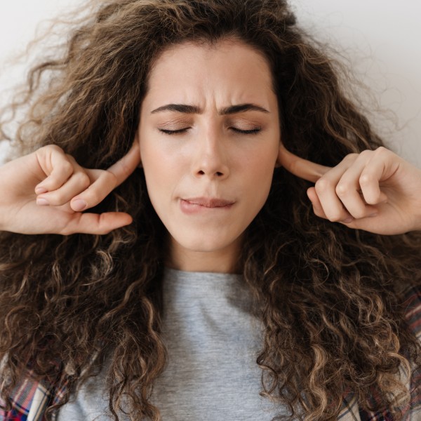 Foto einer unzufriedenen schönen Frau, die sich die Ohren zuhält, während sie vor einer Kamera posiert, isoliert vor weißem Hintergrund